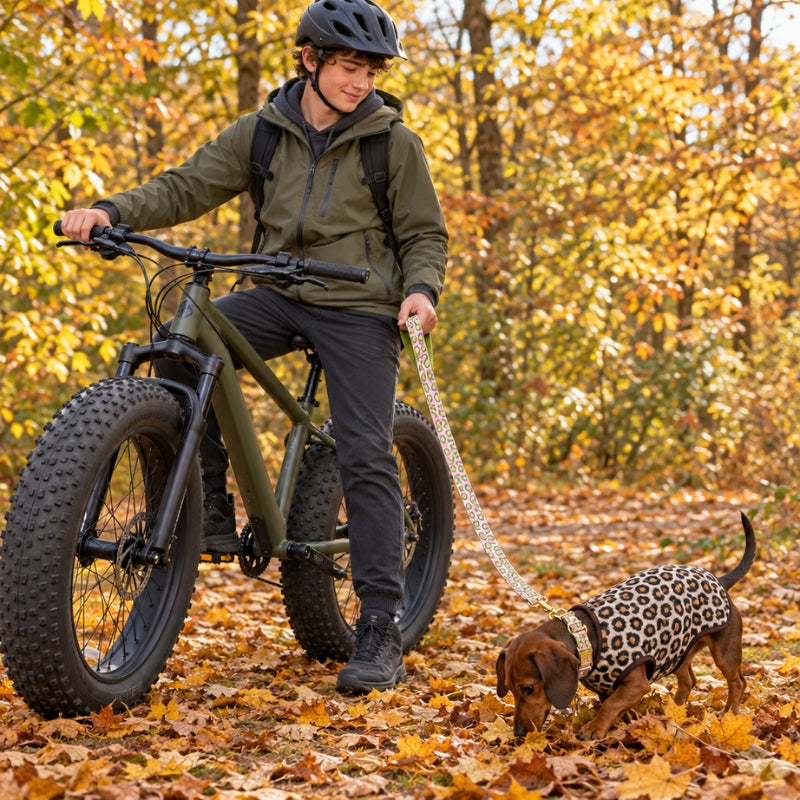 Laisse randonnée chien rose à motifs avocats adolescent sur fat bike tenant un teckel en manteau léopard dans les feuilles